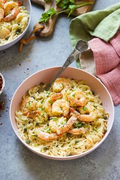 two bowls filled with pasta and shrimp on top of a table