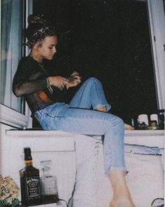 a black and white photo of a woman sitting on a window sill next to a bottle