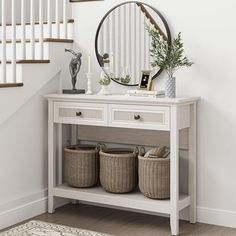 a white console table with baskets under it and a round mirror on the wall above