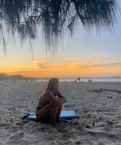 a woman sitting on top of a blue surfboard under a tree at the beach