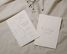 two baby shower cards sitting on top of a bed