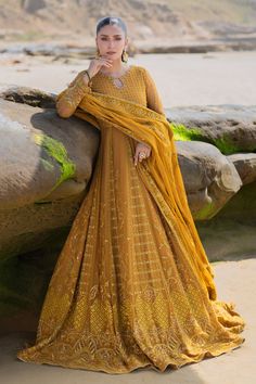 a woman standing on top of a beach next to a large stone wall wearing a yellow dress