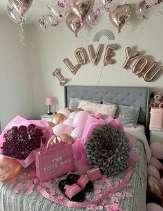 a bed topped with lots of pink and gold balloons in the shape of i love you