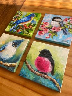 four paintings of birds on canvases sitting on a wooden table next to each other