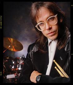 a man with long hair wearing glasses and holding drums