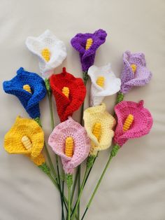 crocheted flowers are arranged on a white surface with green stems in the foreground