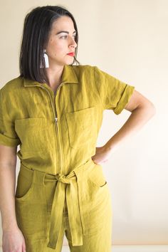 a woman with her hands on her hips wearing a yellow jumpsuit and white earrings