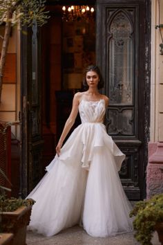 a woman standing in front of a doorway wearing a white dress with ruffles