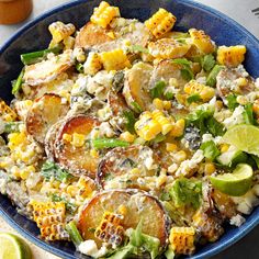 a blue bowl filled with corn and potato salad on top of a table next to lime wedges