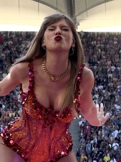 a woman in a red and gold outfit with her hands out to the side as she sings