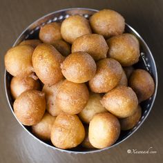 a metal bowl filled with lots of doughnuts on top of a wooden table