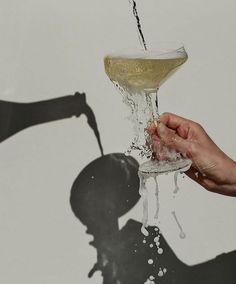 the shadow of a person holding a wine glass in front of a white wall with water pouring out of it