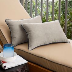 two pillows sitting on top of a couch next to a cup