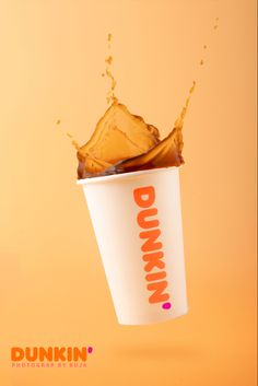 a dunkin'donut falling into a cup filled with liquid on an orange background