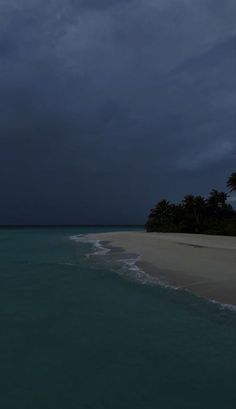 the ocean is blue and green with white sand, palm trees, and dark clouds