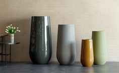 four different colored vases are lined up on the floor next to a small table