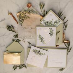 the wedding stationery is laid out with greenery and gold foil on it's envelopes