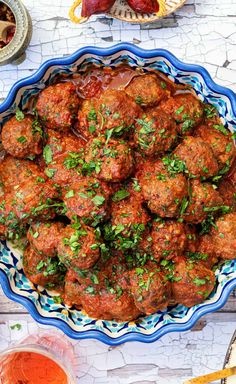 meatballs with parsley in a blue and white dish on a table next to other food