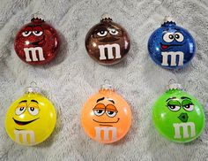 four different colored m and m ornaments on a white blanket, with eyes drawn on each ornament