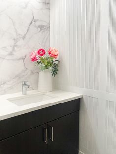 a bathroom with marble walls and black cabinetry has flowers in a white vase on the counter