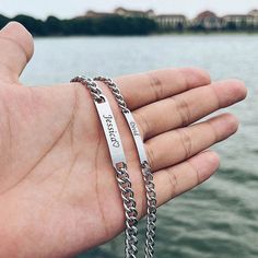 a person is holding two silver bracelets with the words jesus christ on them in front of a body of water