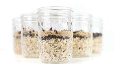 three glass jars filled with granola on top of a white table