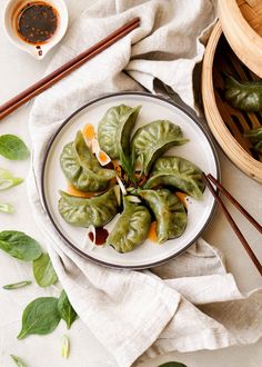 some green leafy vegetables on a plate with chopsticks and dipping sauce in the bowl