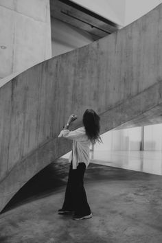 black and white photograph of woman standing in front of large concrete structure with hand on hip