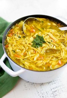 a white pot filled with noodles and carrots on top of a green cloth next to a spoon