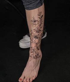 a woman's foot with flowers and leaves on her left side, in front of a black background