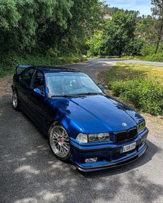 a blue car parked on the side of a road next to some bushes and trees