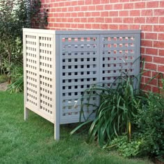 an outdoor privacy panel next to a brick wall with plants in the foreground and green grass on either side