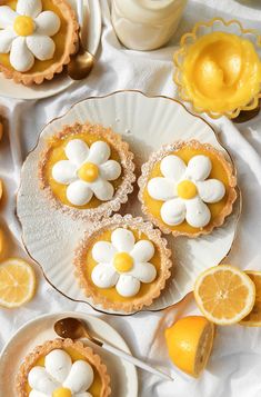 lemon tarts with white and yellow flowers on them sitting on plates next to sliced lemons