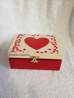 a red and white box with a heart painted on the lid sitting on a bed