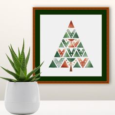 a potted plant sits in front of a cross - stitch christmas tree