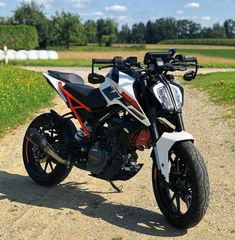 a white and black motorcycle parked on top of a dirt road next to a field