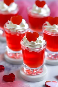 small cups filled with red liquid and topped with heart shaped candies on a table