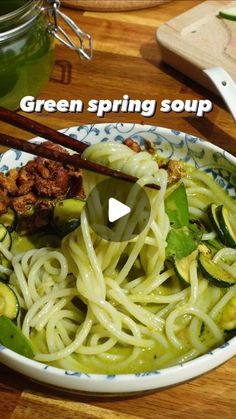 a bowl filled with noodles and vegetables on top of a wooden table next to chopsticks