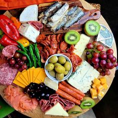 an assortment of cheeses, meats and vegetables on a wooden platter