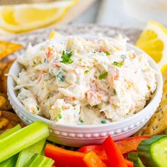 a white bowl filled with crab salad surrounded by crackers and vegetables