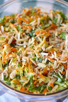 a glass bowl filled with shredded carrots, broccoli and other food items