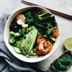 a white bowl filled with vegetables and shrimp next to chopsticks on a table