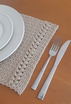 a white plate, fork and knife sitting on top of a placemat next to a crocheted napkin