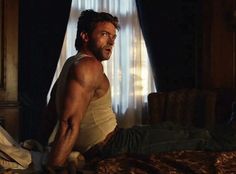 a shirtless man sitting on top of a bed in a bedroom next to a window