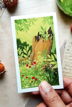 a person holding up a card in front of a tree stump with flowers and leaves on it