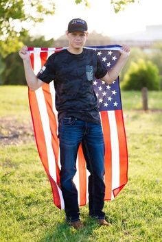 a young man holding an american flag in the grass with his hands on his hips