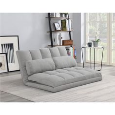 a gray couch sitting on top of a wooden floor next to a book shelf filled with books