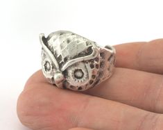 a hand holding a silver ring with an owl on it