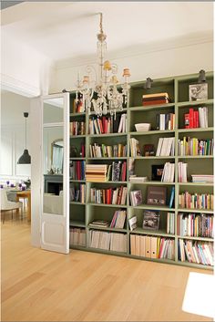 a book shelf filled with lots of books on top of a hard wood floor next to a dining room table