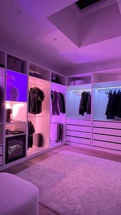 a bedroom with purple lighting and clothes on the closet doors, in front of a white couch